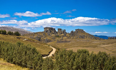 A scenic view of Cumbe Mayo in Cajamarca, Peru, featuring a rugged rock forest, winding trails, and a deep blue sky with scattered clouds.