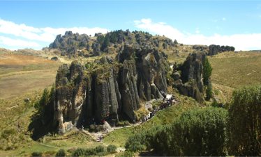 A scenic view of the Cumbemayo archaeological site in Cajamarca, Peru, featuring towering rock formations and a group of tourists exploring the area.