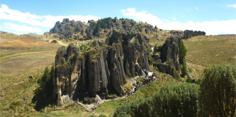 A scenic view of the Cumbemayo archaeological site in Cajamarca, Peru, featuring towering rock formations and a group of tourists exploring the area.