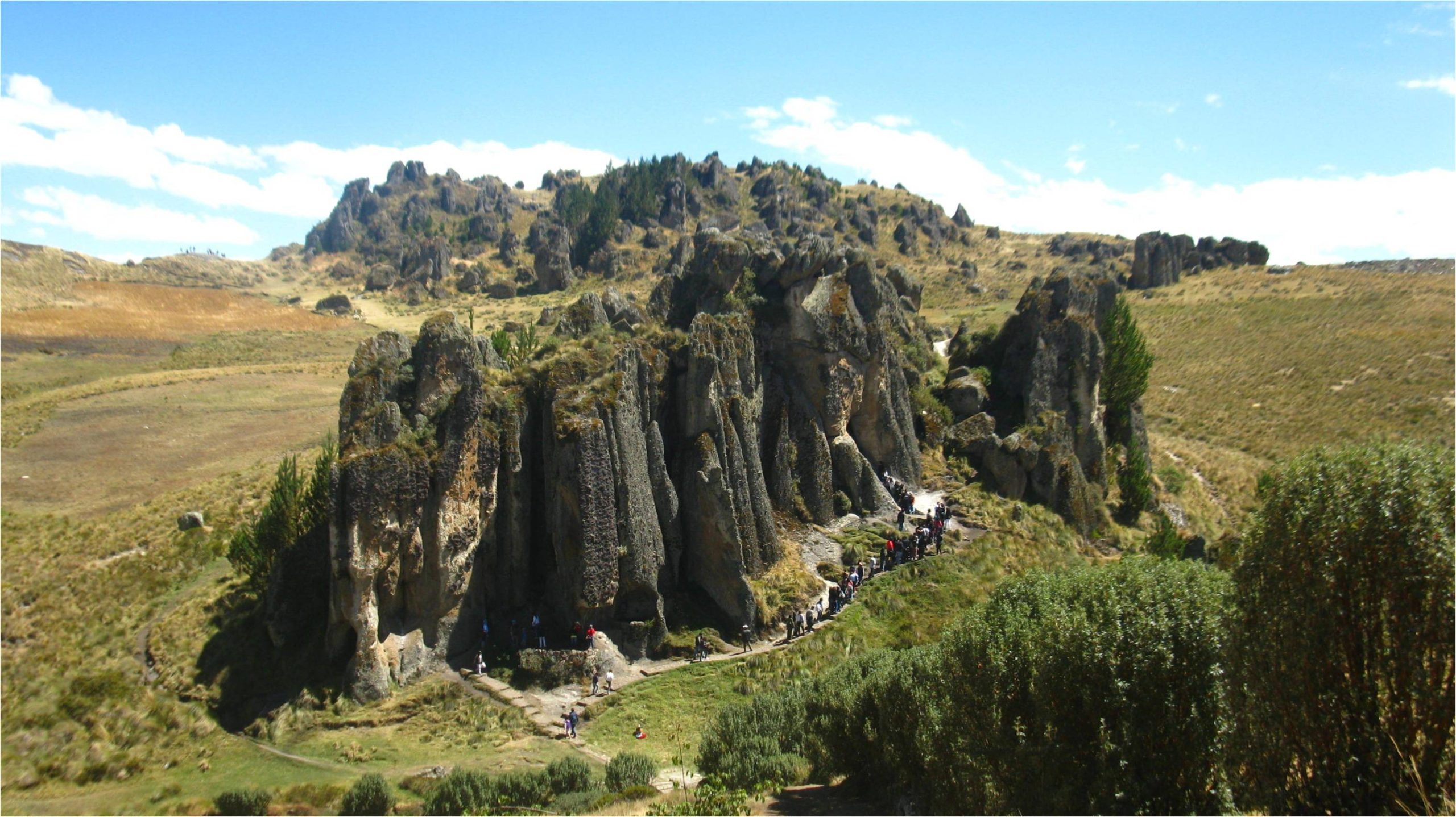 A scenic view of the Cumbemayo archaeological site in Cajamarca, Peru, featuring towering rock formations and a group of tourists exploring the area.