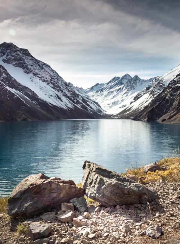 Salkantay Lake surrounded by snow-capped mountains with crystal-clear waters and a partially cloudy sky.