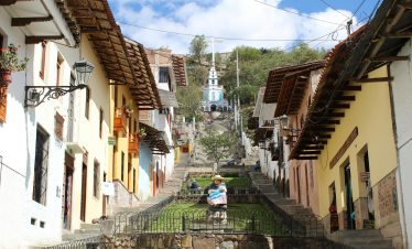 A charming colonial-style street in Cajamarca, Peru, leading up to the Santa Apolonia Chapel, with colorful houses, wooden balconies, and a stone staircase.