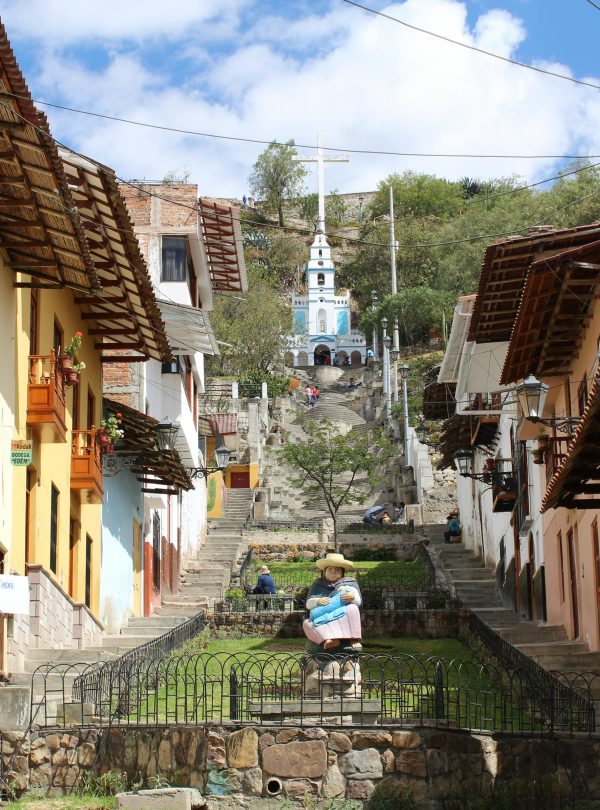 A charming colonial-style street in Cajamarca, Peru, leading up to the Santa Apolonia Chapel, with colorful houses, wooden balconies, and a stone staircase.