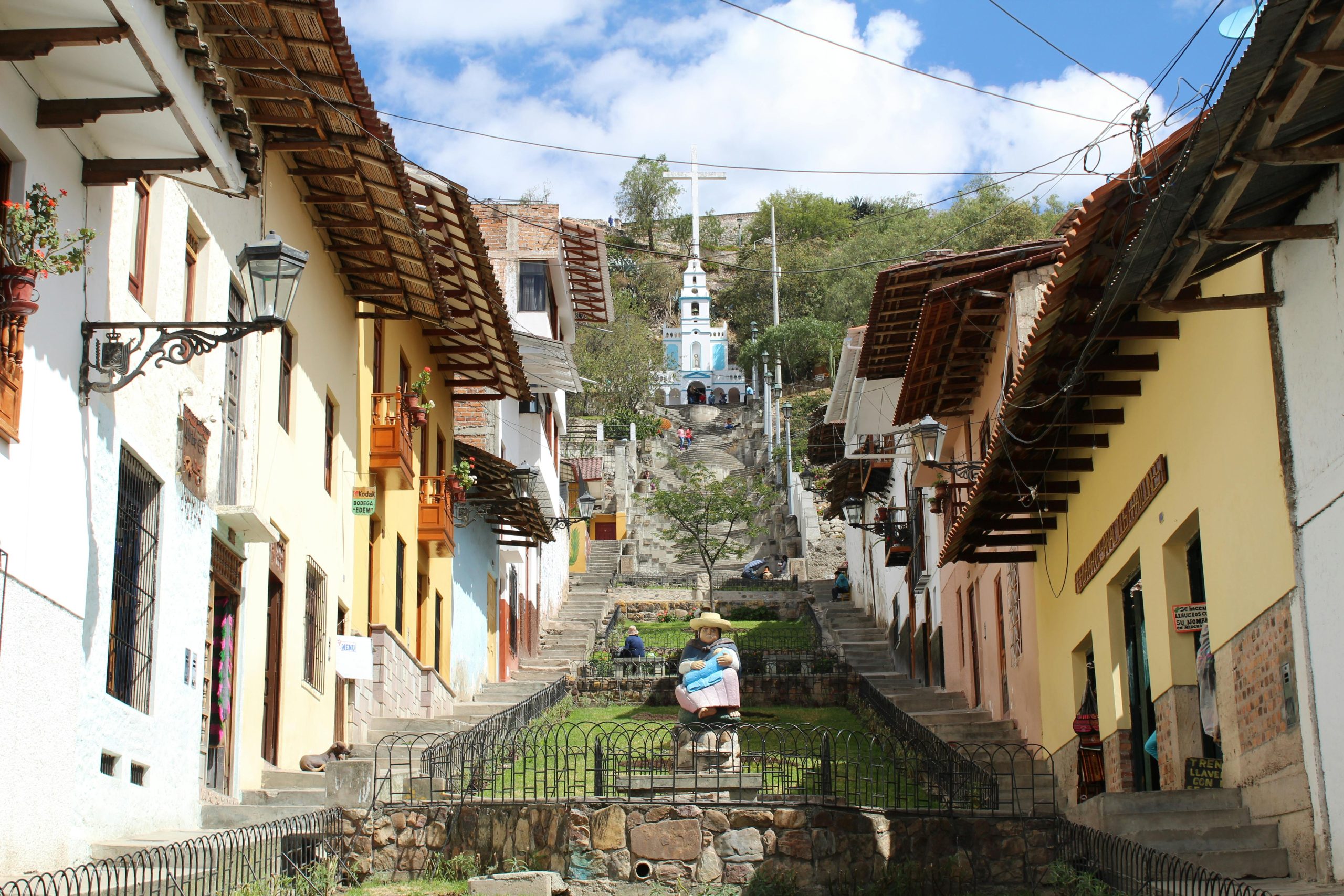 A charming colonial-style street in Cajamarca, Peru, leading up to the Santa Apolonia Chapel, with colorful houses, wooden balconies, and a stone staircase.