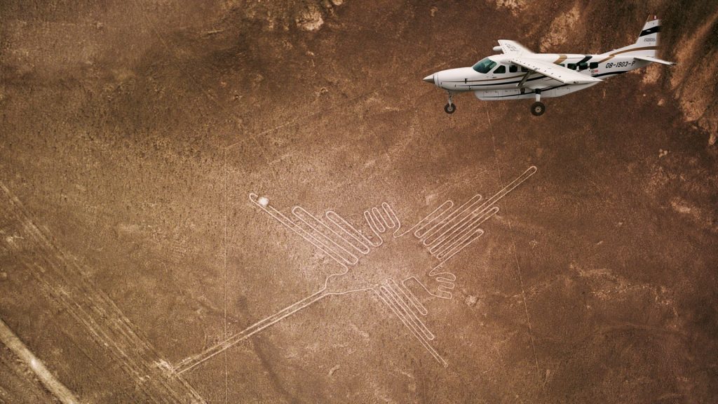 A small airplane flying over the ancient Nazca Lines geoglyphs in the desert.