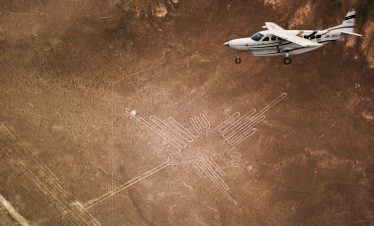 A small airplane flying over the ancient Nazca Lines geoglyphs in the desert.